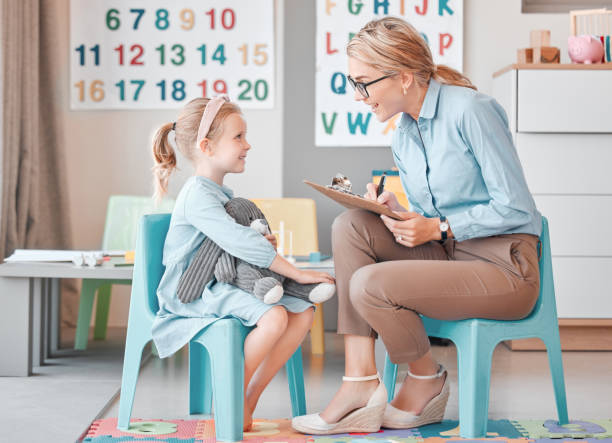 jeune psychologue pour enfants caucasien souriant assis avec une adorable petite fille dans une clinique et utilisant un presse-papiers pour une consultation. fille mignonne parlant à un professionnel de la santé mentale. dyslexie et anxiété - dyslexia & autism photos et images de collection